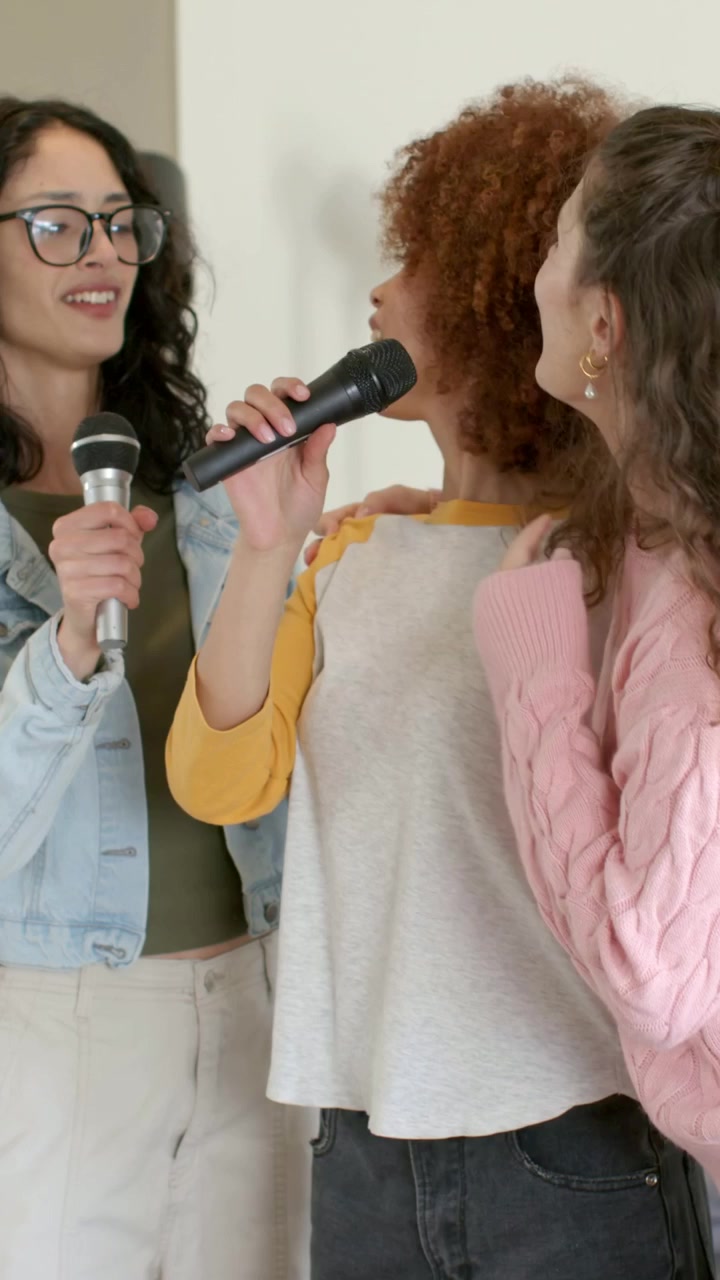 Video verticale: Donna che canta con un maglione rosa, inizia un singalong con gli amici usando microfoni neri a casa.