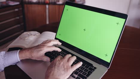 top view shot of old writer's hands typing on computer keyboard at home office, senior author preparing narrations edition and publication, man working on laptop with green screen chroma key mockup