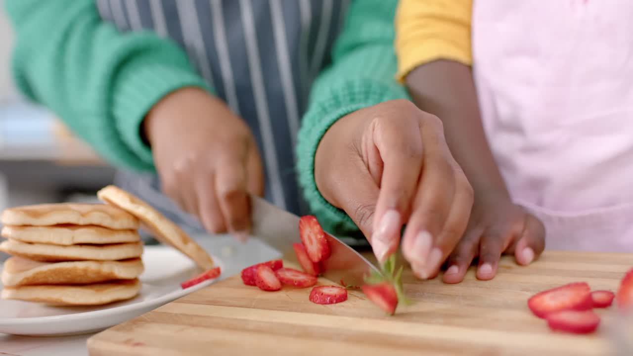 de manos afroamericanas madre e hija cortando frutas en la cocina, cámara lenta