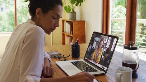 Mujer-Afroamericana-Tomando-Notas-Mientras-Realiza-Una-Videollamada-En-Una-Computadora-Portátil-En-Casa