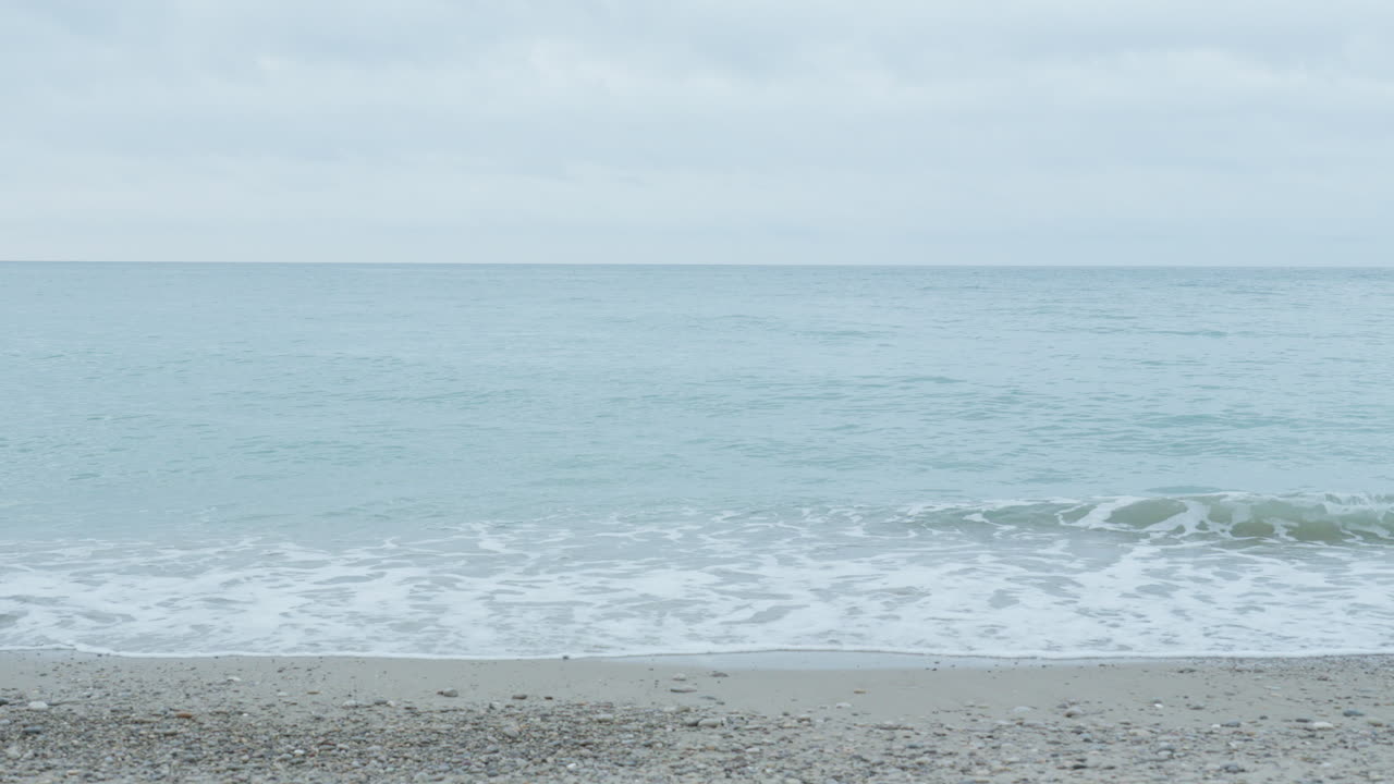 부드러운 바다 파도가 조용한 회색 아침에 해변을 만지고 있습니다.