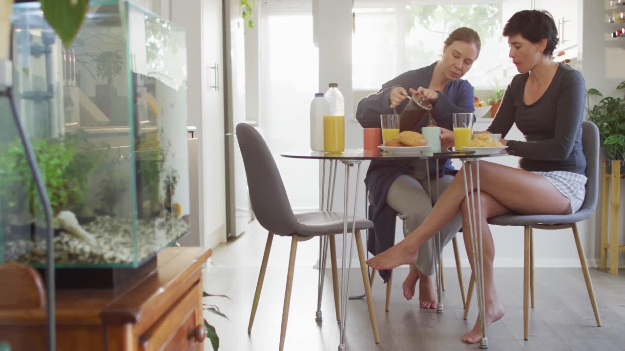 mujer caucásica vertiendo café mientras desayuna con su esposa en casa