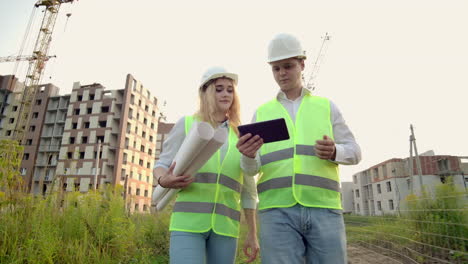 dos ingenieros industriales usan casco de seguridad y sostienen la ingeniería de tableta trabajando y hablando con la inspección de dibujos. en la construcción afuera. herramientas de ingeniería.