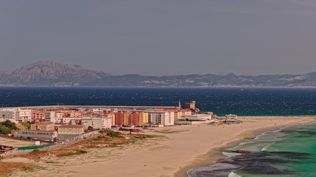 Orbita cinematografica con drone teleobiettivo intorno a Tarifa, Spagna, con una drammatica compressione dell'obiettivo che rivela il Jebel Musa in Marocco che si erge attraverso lo Stretto di Gibilterra sopra la costa atlantica.