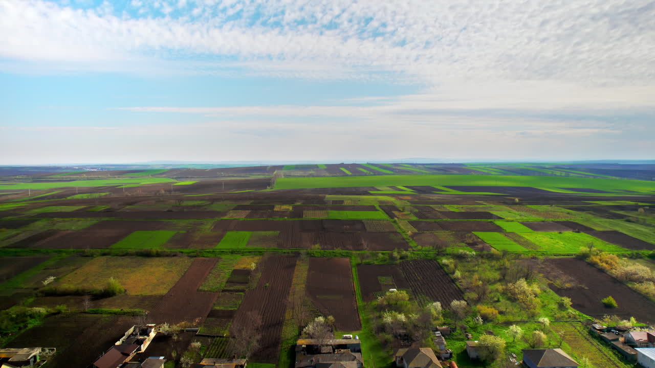 Aerial drone view of a village in Moldova. Multiple residential buildings, green fields around, cloudy sky