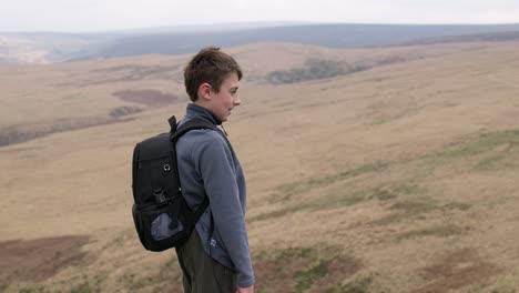 Young-boy-outdoors-standing-on-a-countryside-hill-top,-admiring-the-moorland-views