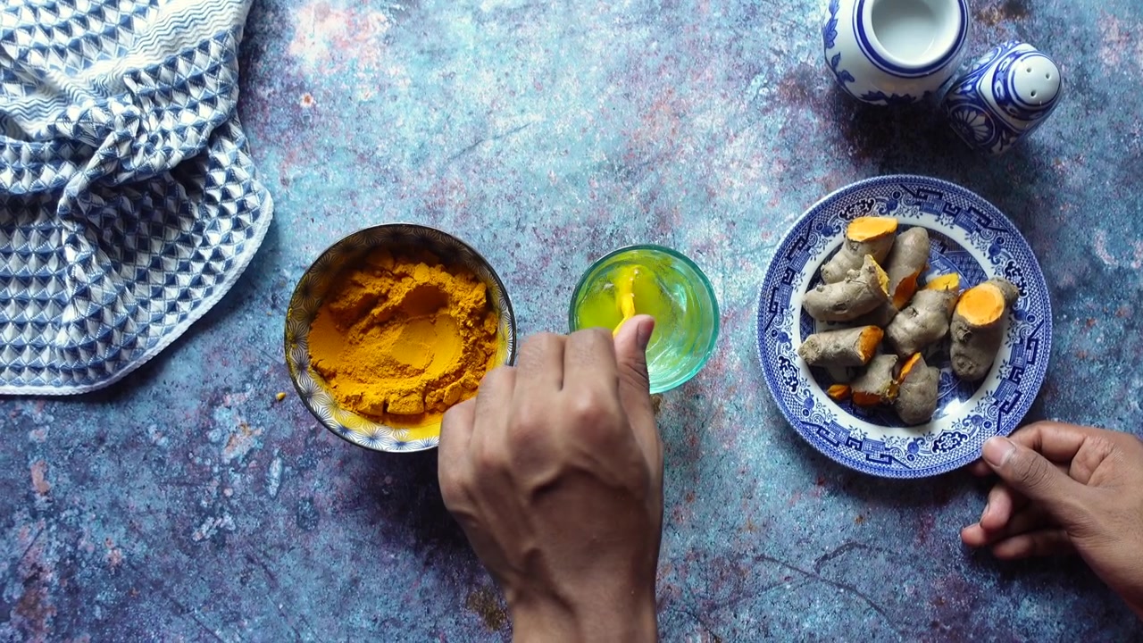 Person Mixing Turmeric Powder into Water in a Glass
