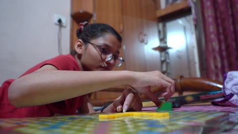 chica con anteojos colocando fichas de letras scrabble en el tablero de juego de la casa - primer plano, tiro de ángulo bajo