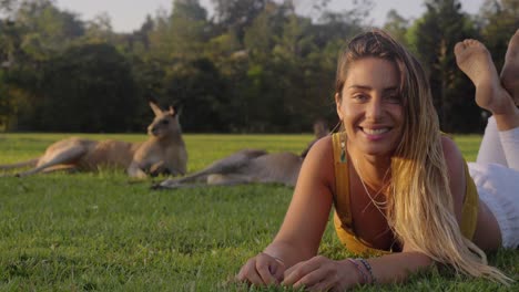 Girl-Smiling-At-Camera-While-Comfortably-Lying-On-The-Green-Grass-Together-With-Eastern-Grey-Kangaroos---Gold-Coast,-QLD,-Australia