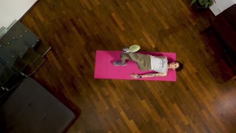 una mujer en una alfombra de yoga rosa está realizando está haciendo un puente de cadera y pone su pierna para el fortalecimiento del núcleo