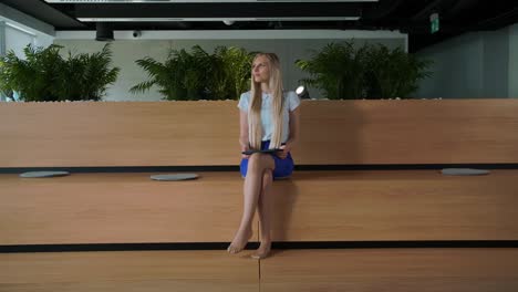 mujer relajada con tableta en la oficina. joven mujer elegante sentada descalza en una tribuna de madera en una oficina moderna usando tableta y descansando