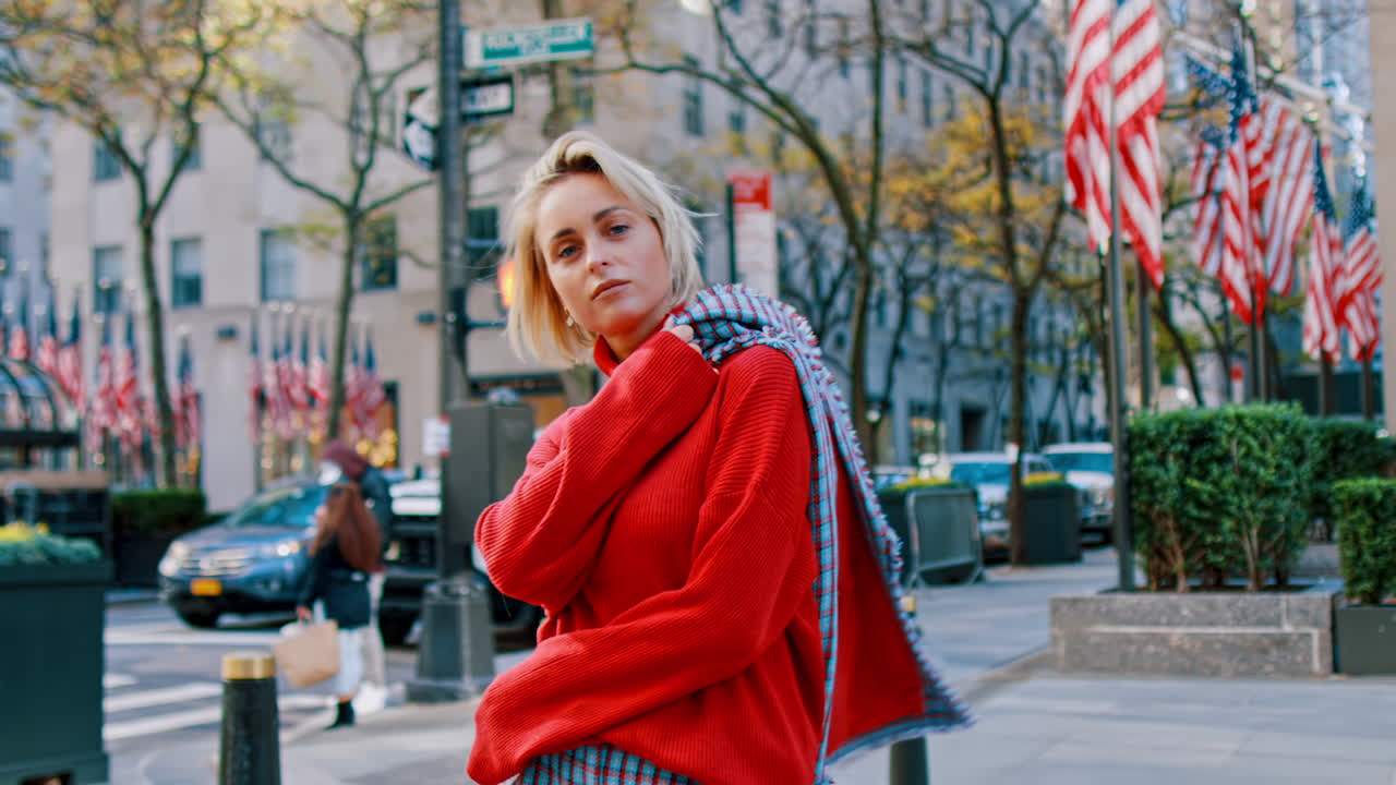 Nueva York, EE. UU., 2 de abril de 2026: Retrato de mujer con cuello alto rojo en una calle de Nueva York. Primer plano de mujer rubia con suéter de cuello alto rojo brillante caminando por una acera en Manhattan cerca de Rockefeller.