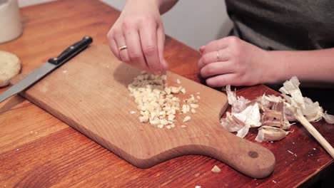 woman's hands salt garlic and crushes with a knife on a chopping board