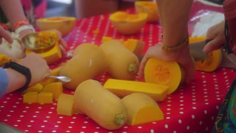 clase de cocina con jóvenes estudiantes cortando calabaza y sacando las semillas con cucharas enormes para hacer una sopa preparando la verdura en una mesa roja con puntos blancos cerca de las manos