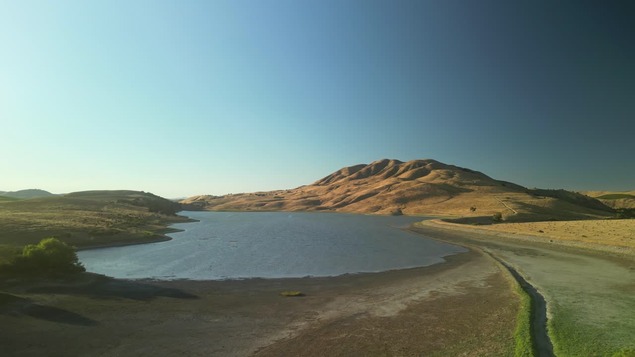 Drone footage glides over Paicines Reservoir, showcasing still waters blending into the surrounding natural landscape.
