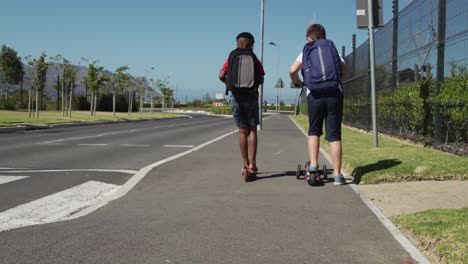 Two-boys-with-school-bags-riding-scooters-on-footpath