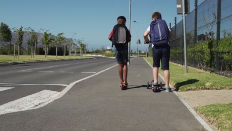 two boys with school bags riding scooters on footpath