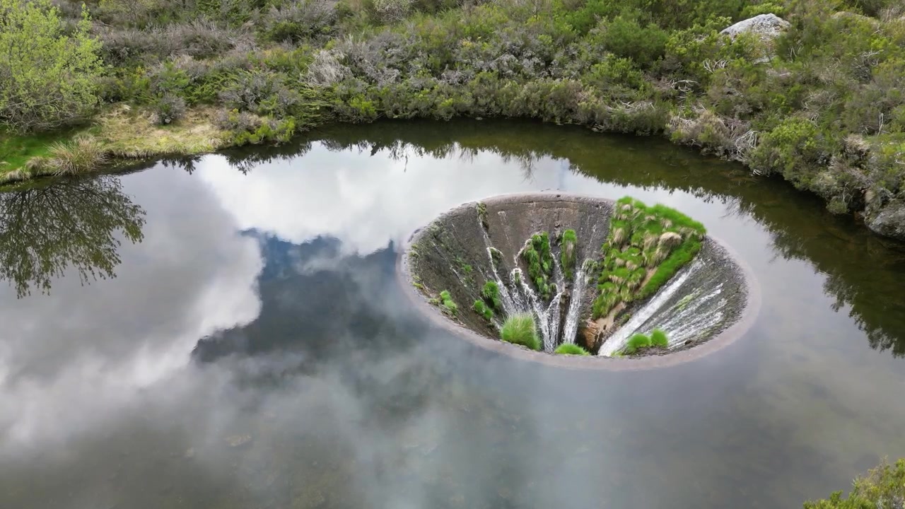 Luftdroneoptagelser af Covão dos Conchos, Portugal: bjergsø med et unikt cirkulært overløb omgivet af Serra da Estrela-landskabet. Ideel til rejse- og naturprojekter.
