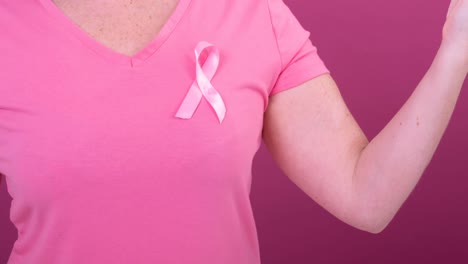 Video-of-midsection-of-caucasian-woman-wearing-pink-cancer-awareness-ribbon,-with-pink-background