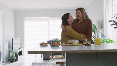 Caucasian-lesbian-couple-embracing-and-smiling-in-kitchen