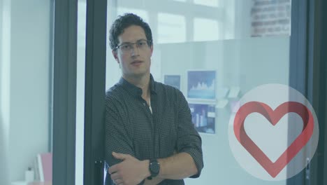 Heart-icon-over-round-banner-against-portrait-of-caucasian-man-with-arms-crossed-smiling-at-office