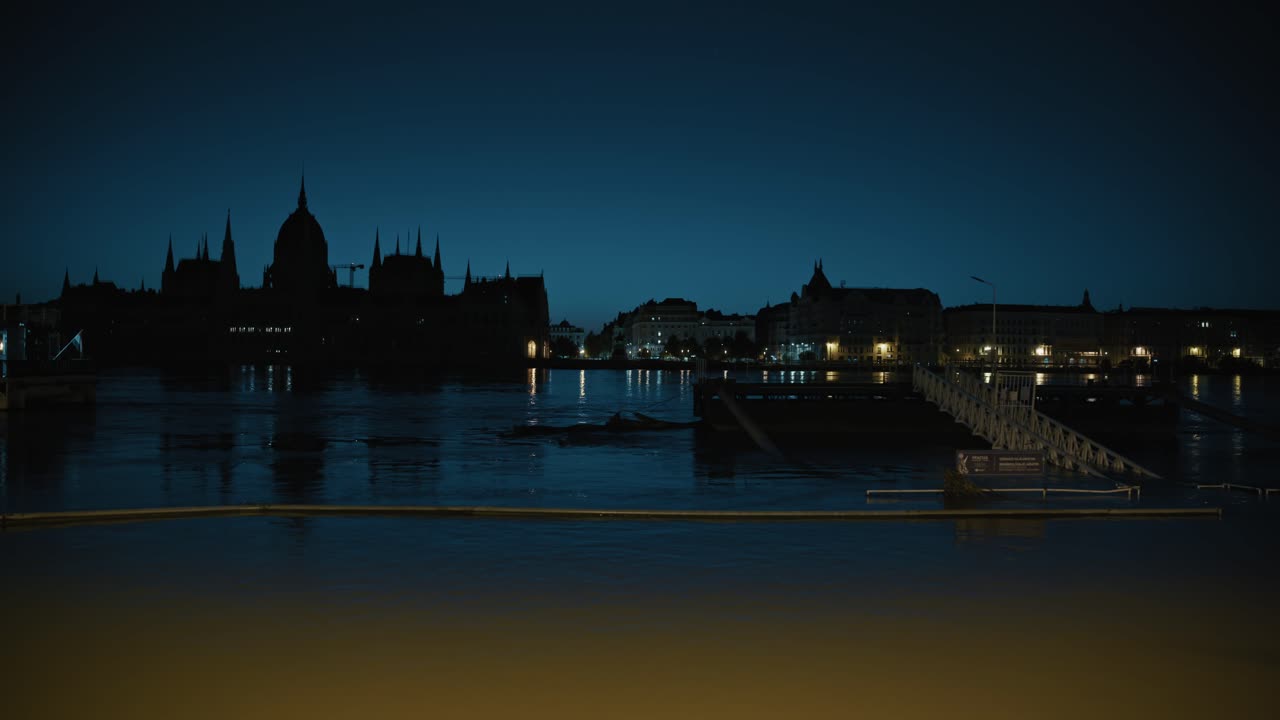 Night view of flooded riverbank with silhouette of Parliament building, Budapest Flood 2024