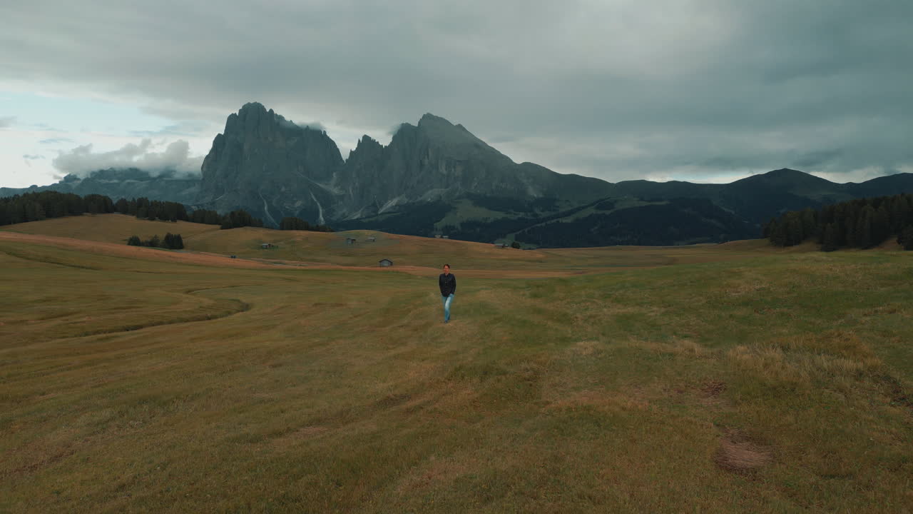 Tourist walking in the meadow with Sassolungo mountain range in the background in Alpe di Siusi, Dolomites, Italy