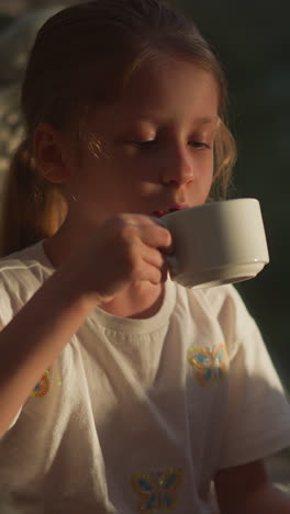 child drinks hot chocolate sitting in furry chair. cute little girl with ponytail closes eyes enjoying pleasant taste of sweet drink at home