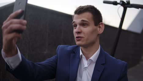 Atractivo-Hombre-De-Negocios-Sentado-En-Las-Escaleras-Y-Chateando-Por-Video-En-Un-Teléfono-Inteligente-Afuera.-Hombre-Con-Elegante-Traje-Azul-Teniendo