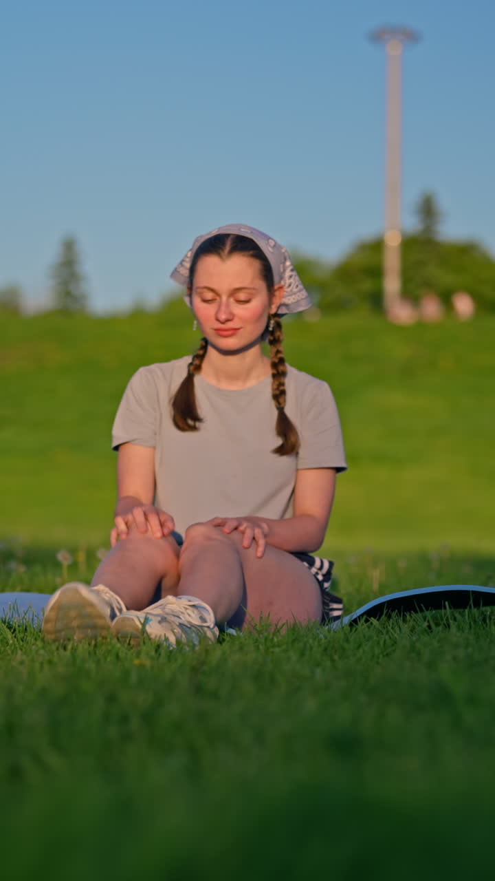 A Gen Z woman practices mindful breathwork in a peaceful park, enjoying a calm digital-detox moment as she settles into a meditative pose and smiles with inner peace. Vertical 4K dolly shot
