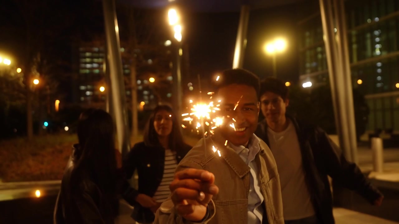 Giovane uomo felice e amici che festeggiano con stelle filanti di notte.