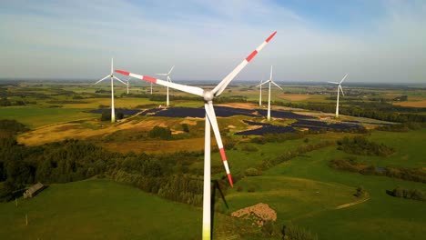 Luftaufnahmen-Von-Solaranlagen-Und-Windkraftanlagen-In-Einem-Windpark,-Der-An-Einem-Sonnigen-Tag-Auf-Einer-Weiten-Grünen-Wiese-In-Taurage,-Litauen,-Grünen-Strom-Erzeugt,-Heranzoomen,-4K