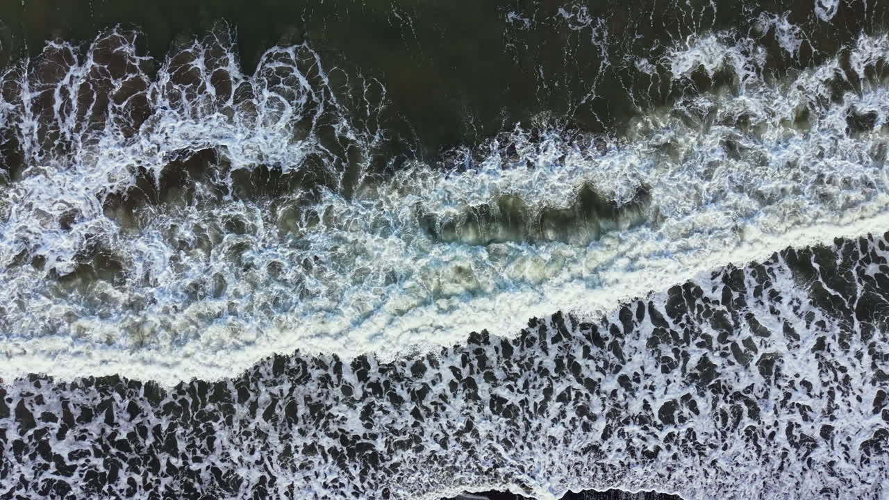 Waves crash on a dark beach with foam and spray showing movement and energy of the water during daytime