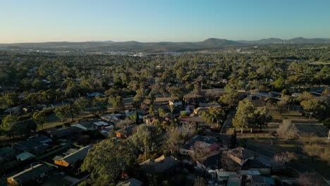 drone ascends from rivett homes, revealing the city skyline far away with soft golden tones blanketing the horizon