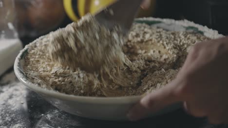 person mixing batter with rolled oats using a wooden spoon