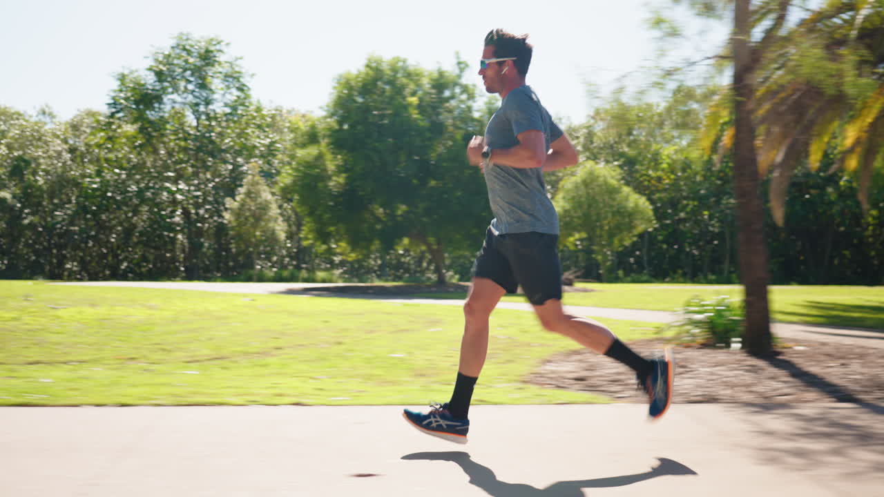 화창한 날 공원 보도에서 조깅하는 선글라스를 쓴 남자의 옆모습, 4k 느린 동작