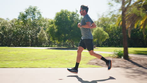 Seitenprofil-Eines-Mannes-Mit-Sonnenbrille,-Der-An-Einem-Sonnigen-Tag-Auf-Einem-Parkweg-Joggt,-4k-Zeitlupe