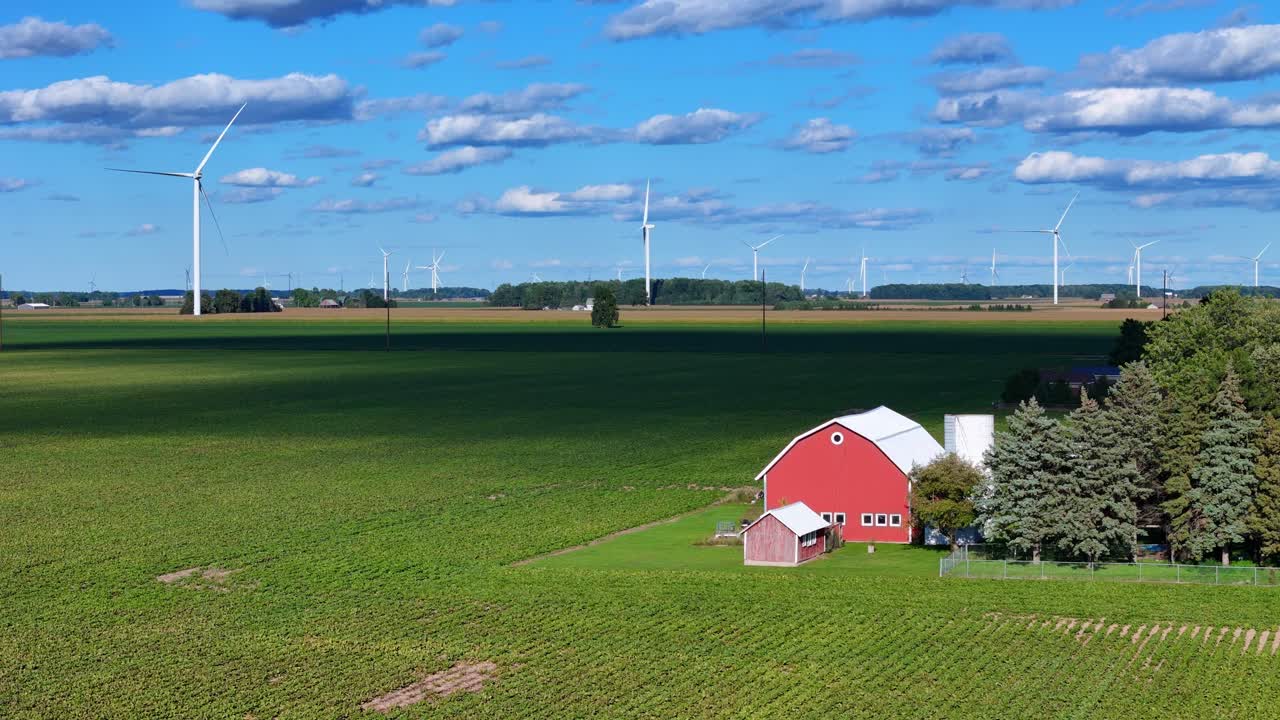 Vindmøller, der genererer ren elektricitet på en bred mark med en klassisk rød lade og skyer på det amerikanske landskab.
