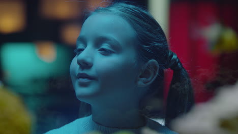 happy girl looking at fish in aquarium curious child watching colorful sea life swimming in tank learning about marine animals in underwater ecosystem inquisitive kid at oceanarium