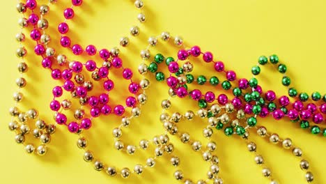 video of pink, gold and green mardi gras carnival beads on yellow background