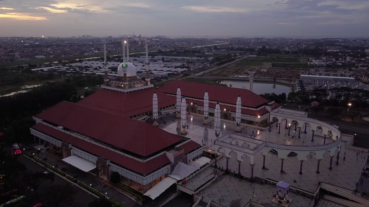 Reveal drone shot of the great Mosque of Central Java (MAJT) in suset time. Th sun is orange and the weather is cloudy. It have some pillars and some umbrela that is closed