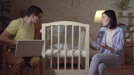 young parents search the internet and a newborn in a baby bed close up