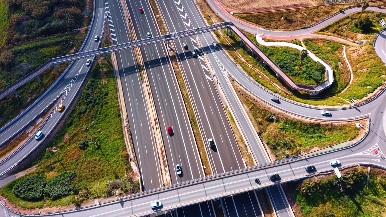 Prospettiva dall'alto di un ponte sopraelevato autostradale, Spagna. Vista verticale diretta di più corsie, traffico in movimento, auto bianche e vegetazione verde a bordo strada.