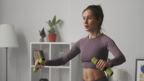 Ama-De-Casa-Está-Haciendo-Deporte-En-Casa-Levantando-Pesas-Con-Ambas-Manos-Entrenando-Su-Cuerpo-Para-Mantenerse-En-Forma-Y-En-Buena-Forma-Retrato-Medio-De-Una-Mujer-Cansada-En-La-Habitación