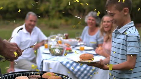 confetti animation over family enjoying outdoor barbecue with boy holding burger