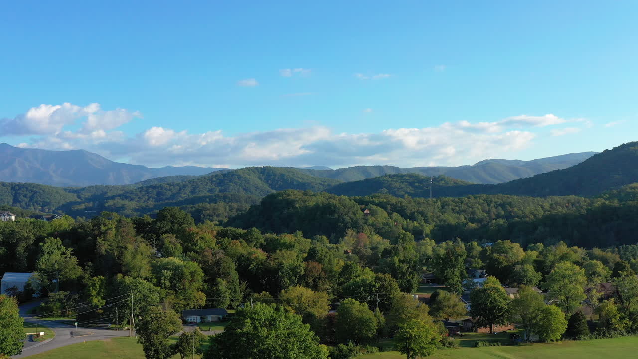 Aerial footage of a drone retreating over a verdant Tennessee landscape, revealing the majestic Great Smoky Mountains. The lush forest and quaint homes fade into the distance