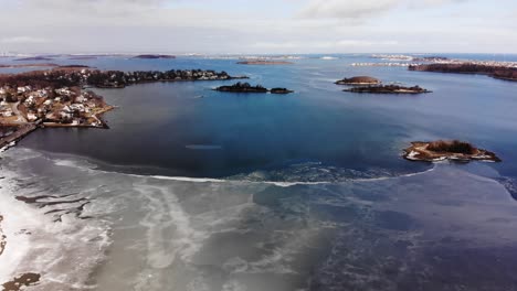 aerial view over a frozen harbor along the coast of a seaside village in winter, wide angle, partly sunny day