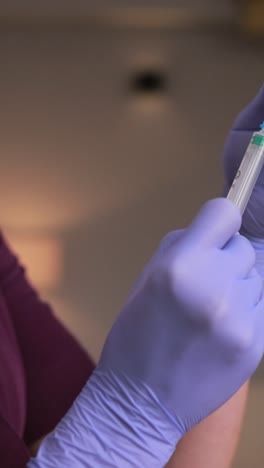the nurse, wearing a purple mask and gloves, is preparing a vaccine with careful gestures using her fingers and thumbs