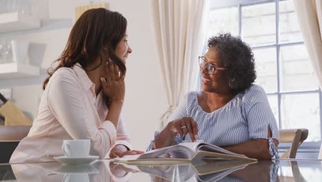 Senior-mixed-race-woman-reading-a-magazine-with-her-daughter,-in-social-distancing