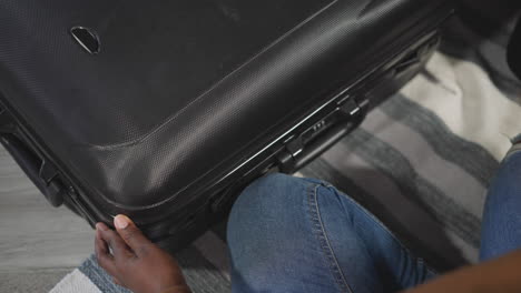 african american woman closes black suitcase with clothes